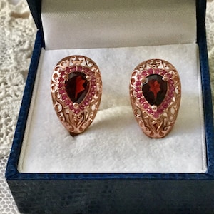 Peut inclure: Une paire de boucles d'oreilles en or rose avec une pierre de grenat en forme de poire entourée de petites pierres roses.