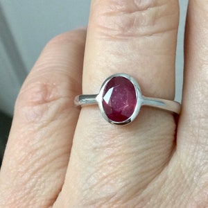 Peut inclure: Une bague en argent avec une pierre ovale rouge. La bague est sur le doigt d'une personne.