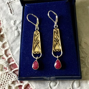 Peut inclure: Une paire de boucles d'oreilles pendantes en argent et or avec des gouttes de pierres précieuses rouges. Les boucles d'oreilles présentent un design délicat et complexe.