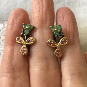 Peut inclure: Une paire de boucles d'oreilles en or avec un motif de trèfle. Les boucles d'oreilles sont serties d'émeraudes vertes et de rubis roses.