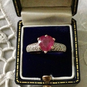 Peut inclure: Une bague en argent avec un rubis en forme de cœur entouré d'une rangée de petits diamants.
