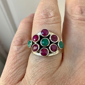 May include: A silver ring featuring a cluster of red and green gemstones. The ring is set with nine round stones, six red and three green.