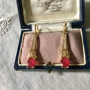 Peut inclure: Une paire de boucles d'oreilles pendantes en or avec des gouttes de pierres précieuses rouges et des accents de cristal transparent. Les boucles d'oreilles sont dans un écrin en velours bleu avec une étiquette qui indique "A. Woodhouse, 36, Carey St., Lincoln's Inn, London."