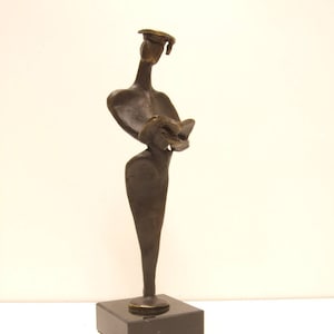 Può includere: Una scultura in bronzo di una persona che tiene un libro. La scultura è su una base di marmo nero.
