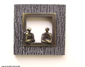 Op de afbeelding: Een vierkant, getextureerd, donkergrijs wandkunstwerk met een bronzen lijst. Binnen de lijst staan twee kleine bronzen figuren. Het wandkunstwerk meet 14x14 cm en heeft de tekst "MA00526SB" onderaan.