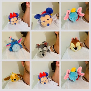 Puede incluir: Se muestran nueve peluches diferentes, cada uno con un personaje popular de Disney, en los hombros de nueve personas diferentes. Los peluches incluyen Mickey Mouse, Minnie Mouse, Dumbo, Stitch, Simba, Lady y algunos otros.