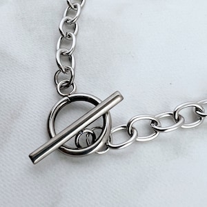 May include: A silver chain necklace with a toggle clasp. The chain is made of thick, linked metal.