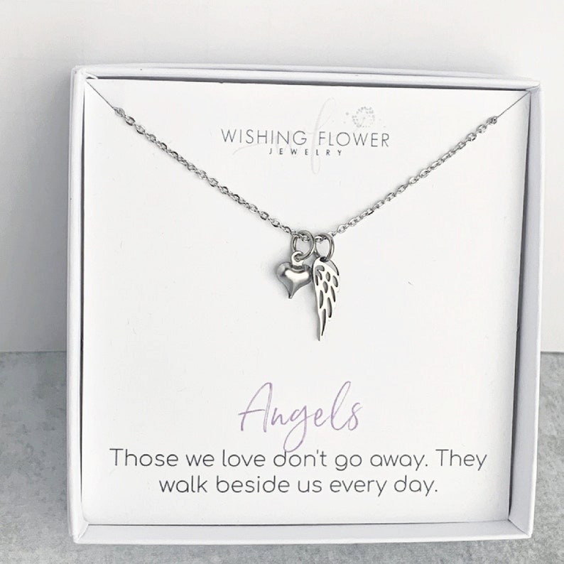 May include: A silver necklace with a small heart and angel wing charm. The necklace comes in a white box with the text "Wishing Flower Jewellery" and "Angels Those we love don't go away. They walk beside us every day."