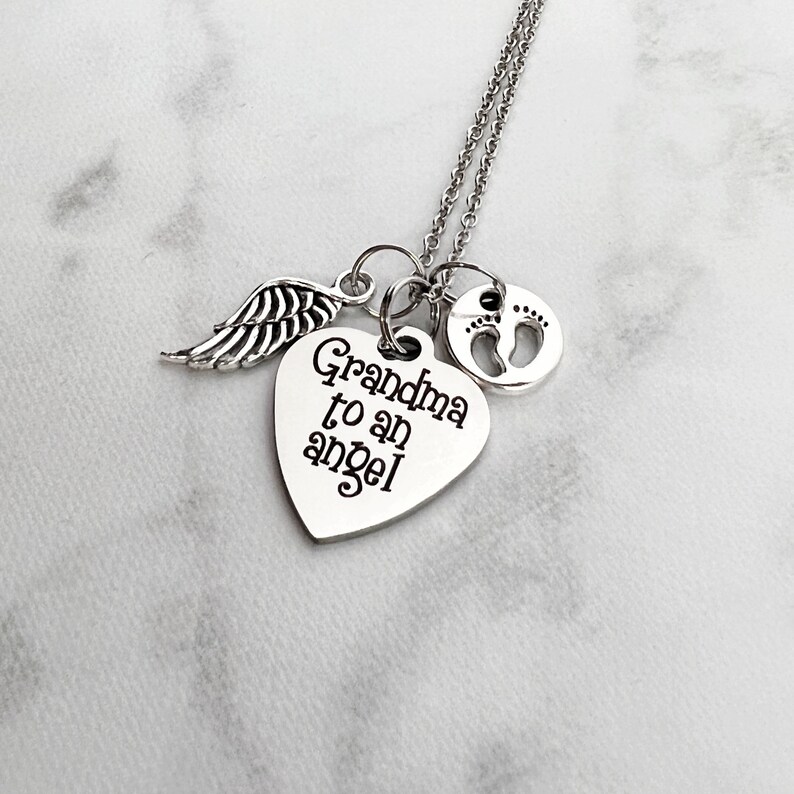 May include: Silver necklace with a heart charm that says "Grandma to an angel" and a small charm with a footprint design. The necklace also has a small angel wing charm.