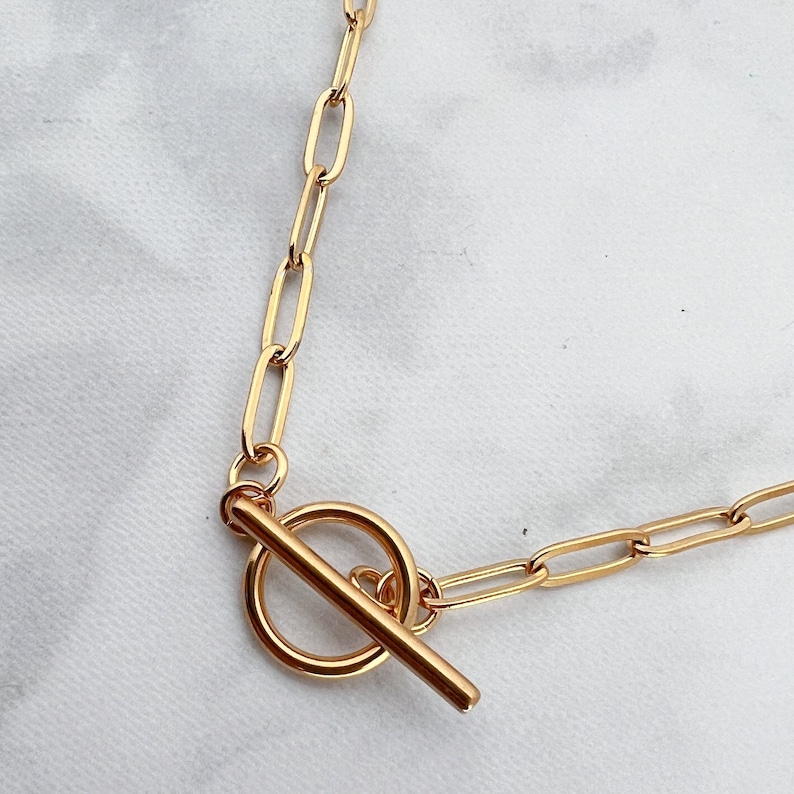 May include: A gold chain necklace with a toggle clasp. The chain is made of oval links.