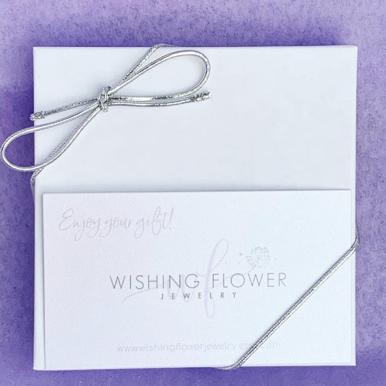 May include: A white gift box with a silver ribbon tied in a bow. The box contains a white card with the text "Enjoy your gift!" and the words "Wishing Flower Jewellery" with a floral design. The website address "www.wishingflowerjewelry.com" is printed at the bottom of the card.