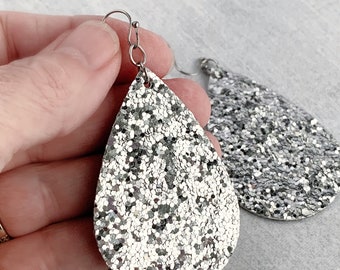 May include: A pair of silver glitter teardrop earrings with silver hooks.