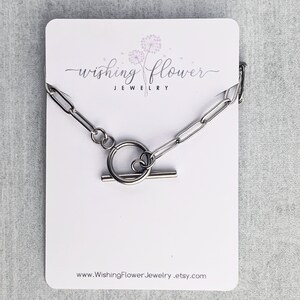 May include: A silver chain necklace with a toggle clasp. The necklace is displayed on a white card with the text "Wishing Flower Jewelry" and the website address "www.WishingFlowerJewelry.etsy.com".
