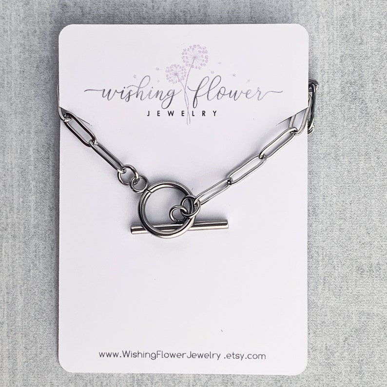 May include: A silver chain necklace with a toggle clasp. The necklace is displayed on a white card with the text "Wishing Flower Jewelry" and the website address "www.WishingFlowerJewelry.etsy.com".