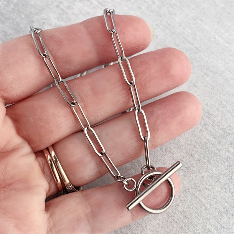 May include: A silver chain necklace with a toggle clasp. The chain is made of oval links.