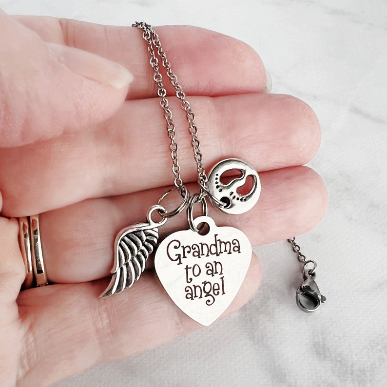 May include: Silver necklace with a heart charm that says "Grandma to an angel" and a small angel wing charm. The necklace also has a small charm with a footprint design.