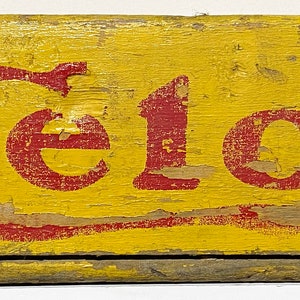 May include: A yellow wooden crate with red lettering that reads "Drink Celo Beverage".