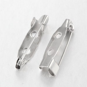 Peut inclure: Deux dos de broche en métal argenté avec une épingle et un fermoir. Les dos sont de forme ovale avec trois trous.