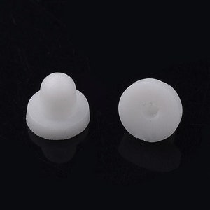 Peut inclure: Deux attaches en plastique blanc. L'une a un dessus arrondi et une base circulaire. L'autre est un disque circulaire avec un petit trou. Les deux sont sur fond noir.