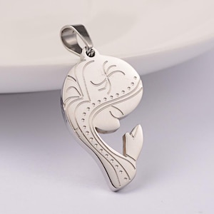 Peut inclure: Pendentif argenté représentant une baleine stylisée. Le pendentif présente des détails gravés et une boucle pour une chaîne. Le corps de la baleine est incurvé, avec une nageoire caudale en bas. Le design comprend des lignes décoratives et de petits points.