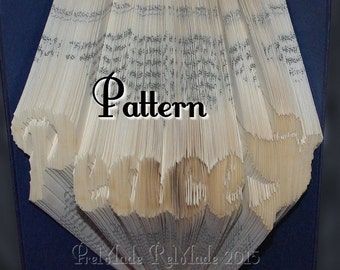 May include: A book folded into the shape of the word "Peace" with a gold ribbon at the bottom. The book is displayed on a blue background with the text "PreMade ReMade 2015" below the book. The word "Pattern" is written in black above the book.