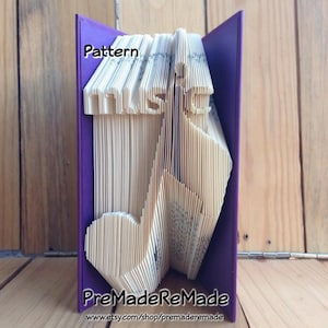 May include: A book art sculpture of a treble clef, folded from the pages of a book. The book is bound in purple fabric and the sculpture is titled "Pattern".