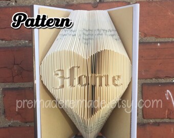 May include: A book folded into the shape of a heart with the word "Home" written inside. The book is open and standing on a wooden surface.