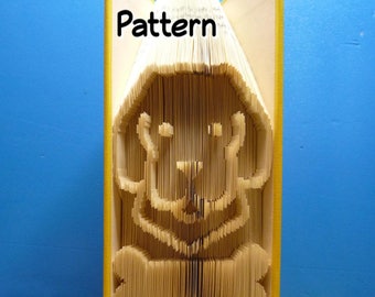 May include: A yellow book with the text "Pattern" on the cover has been folded into a 3D sculpture of a dog. The sculpture is standing on a patterned surface with a ladybug in front of it. The text "PreMadeReMade" and a website address are printed on the bottom of the book.