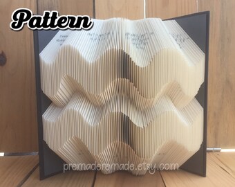 May include: A book art sculpture with a wavy pattern, folded into a three-dimensional design. The book is bound in black and the pages are white. The sculpture is titled "Pattern".