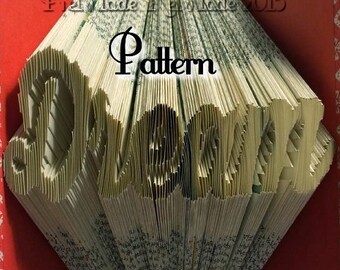 May include: A book with the word "Dream" folded into the pages. The book is open and the pages are folded to create the word. The book is red with a white pattern on the cover.