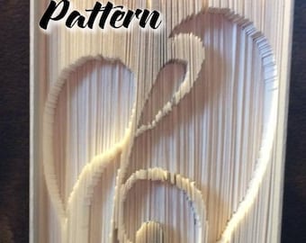 May include: A book folded into the shape of a treble clef and a heart. The book is made of white paper and has the words "Pattern" and "Pre-Made Bookfold" printed on it.