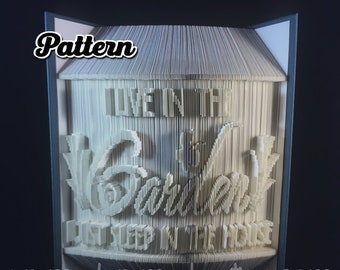 May include: A white book folded into a 3D sculpture of a house with the text "Live in the Garden, Let Sleep in the House".