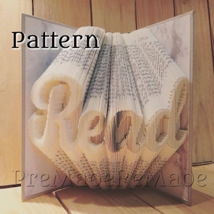 May include: A book art sculpture of the word "Read" made from folded pages. The sculpture is displayed on a wooden surface. The image includes the text "Pattern" and "PreMade/PreMade".