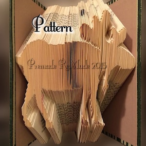 May include: A book transformed into a deer sculpture. The pages are intricately folded and cut to form the shape of a deer. The word "Pattern" is visible on the book's pages. The book's cover is green with a brown interior.
