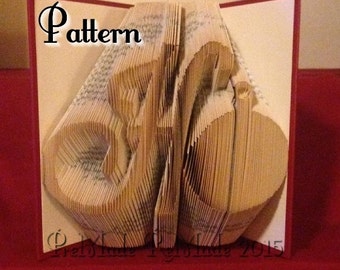 May include: A book art sculpture of the letter "H" made by folding the pages of a book. The sculpture is displayed open on a red surface. The text "Pattern" is visible on the cover of the book.