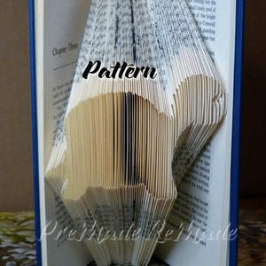 May include: A book art sculpture, folded into the shape of a bird, with the word "Pattern" written in black on the pages. The book is open and the pages are folded into a three-dimensional shape.