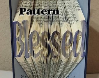 May include: A book art sculpture with the word "Blessed" folded into the pages. The book is decorated with blue paper flowers and a silver ribbon.