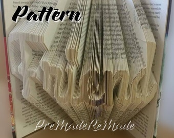 May include: A book art sculpture of the word "FREEDOM" created by folding the pages of a book. The book is open and the pages are folded to create the letters. The word "Pattern" is written in black on the front cover of the book. The book is sitting on a brown surface.