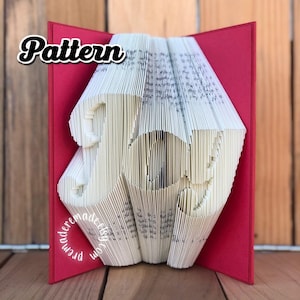 Puede incluir: Un libro rojo con la palabra "Pattern" en letras negras en negrita en la portada. El libro está doblado en forma de la palabra "Joy" en papel blanco.
