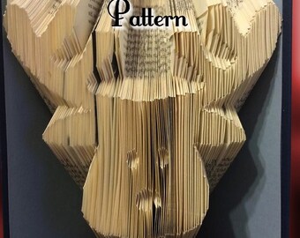 May include: A book sculpture with pages folded into a decorative pattern. The word "Pattern" is visible on the pages. The sculpture is set against a red and gray background.