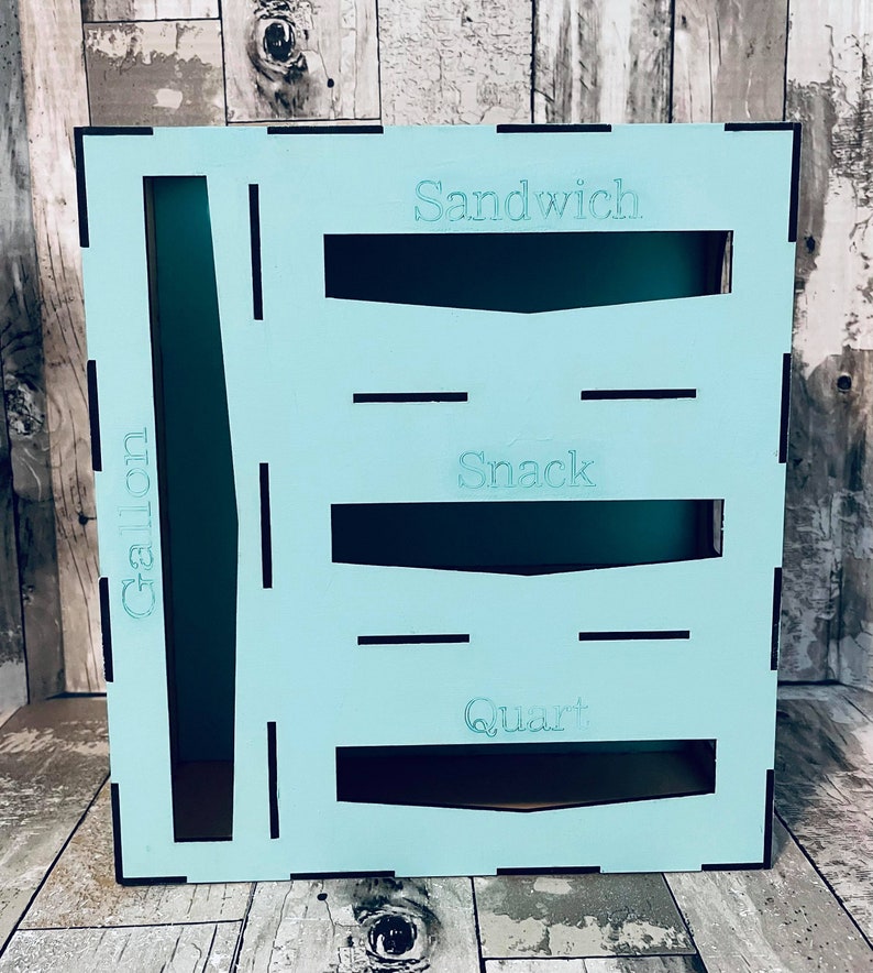 May include: A light blue wooden storage box with cutouts for storing various items. The box has labels for "Sandwich", "Snack", "Quart", and "Gallon".