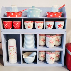 Puede incluir: Una estanter&iacute;a blanca con una variedad de tazas, cuencos y una tetera con patrones rojos y blancos. La estanter&iacute;a est&aacute; llena de utensilios de cocina y est&aacute; colocada sobre una encimera.
