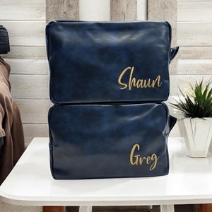 May include: Two blue leather travel bags with gold lettering. The top bag says "Shaun" and the bottom bag says "Greg".