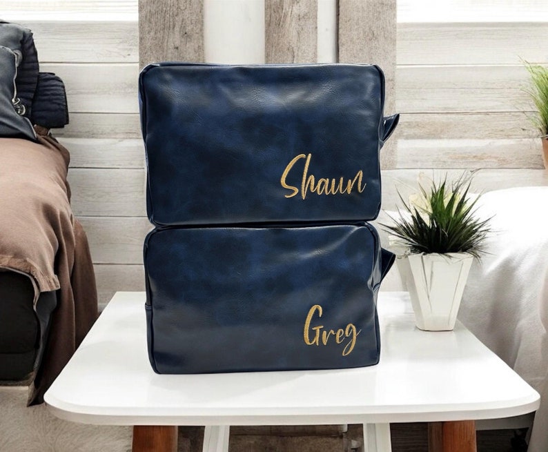 May include: Two blue leather travel bags with gold lettering. The top bag says "Shaun" and the bottom bag says "Greg".