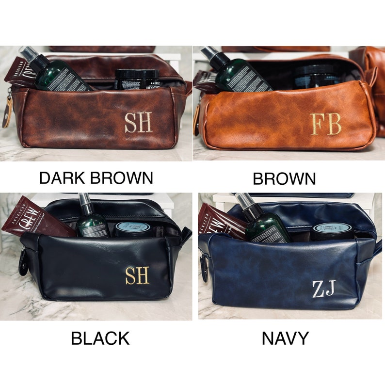 Op de afbeelding: Vier leren toilettassen in donkerbruin, bruin, zwart en marineblauw. Elke tas is rechthoekig met een ritssluiting en bevat verzorgingsproducten. De tassen zijn gepersonaliseerd met goud geborduurde initialen. De tekst geeft de kleur aan.