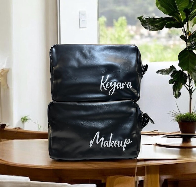 May include: Two black leather zippered cosmetic bags. The top bag has the name "Keyara" embroidered in white. The bottom bag has the word "Makeup" embroidered in white.