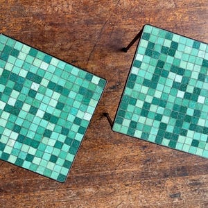 May include: Two square side tables with a mosaic tile design. The tiles are shades of green and white, arranged in a grid pattern. The tables have black metal legs and are set on a wooden surface.