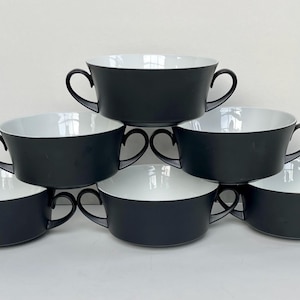 May include: A set of six black and white soup bowls arranged in a pyramid shape. The bowls have a matte black exterior and a bright white interior. Each bowl has two curved handles.