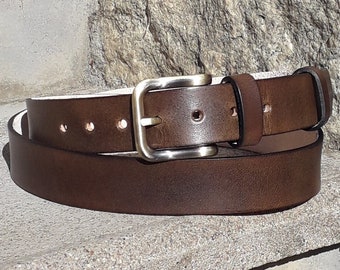 May include: A brown leather belt with a silver buckle. The belt is rolled up and sitting on a stone surface.