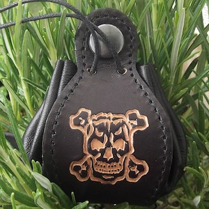 以下が含まれることがあります： 骸骨と交差した骨のデザインが施された黒い革製のポーチ。ポーチは巾着式で、金属製のリングが付いています。